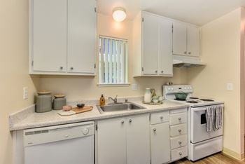 Kitchen with white cabinets and appliances, including dishwasher and stove/oven.